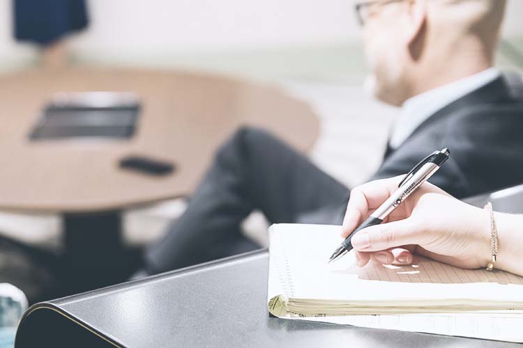 A serious woman looks across the desk at two other people